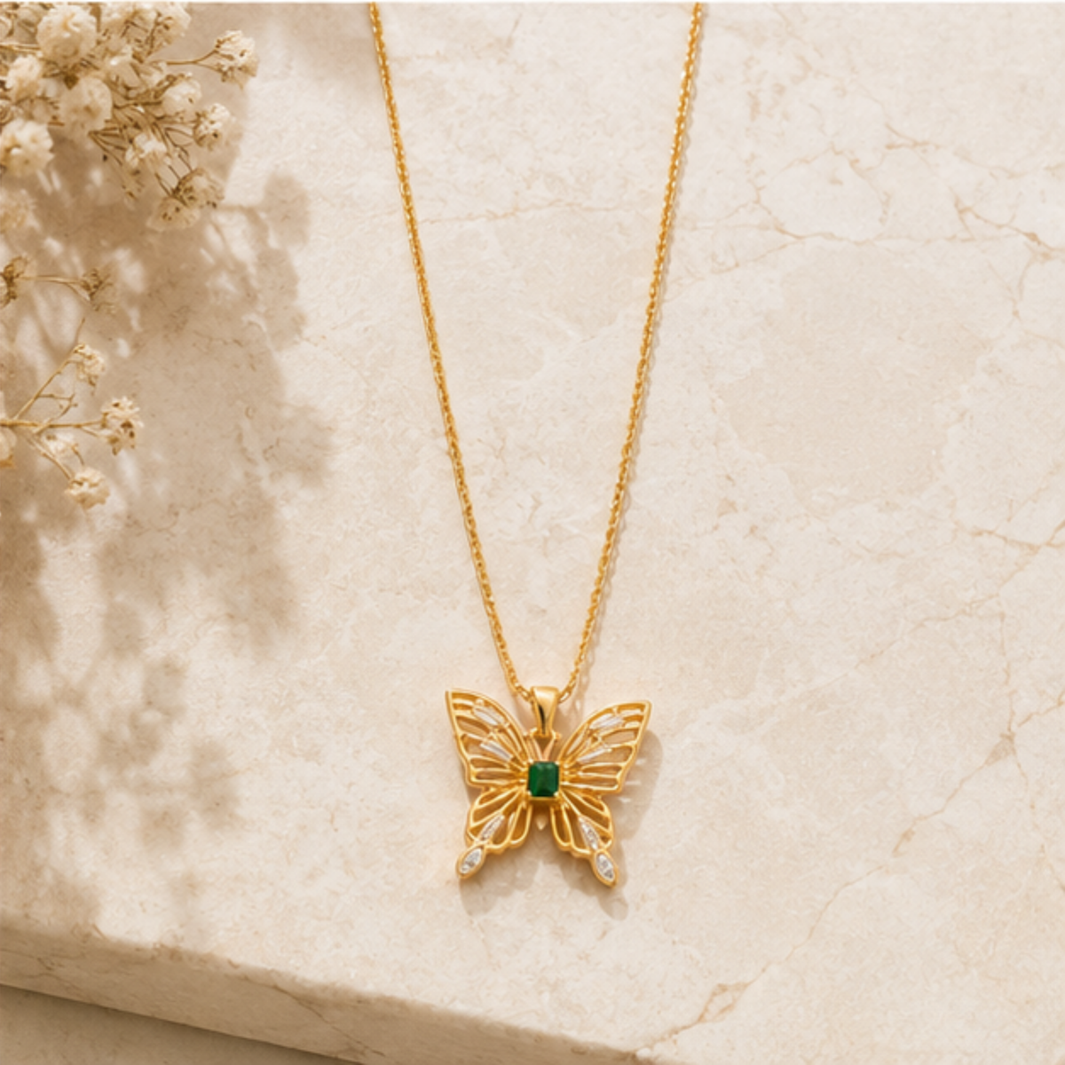 Delicate gold butterfly pendant necklace featuring a green center stone and clear stone wing tips | Maelle